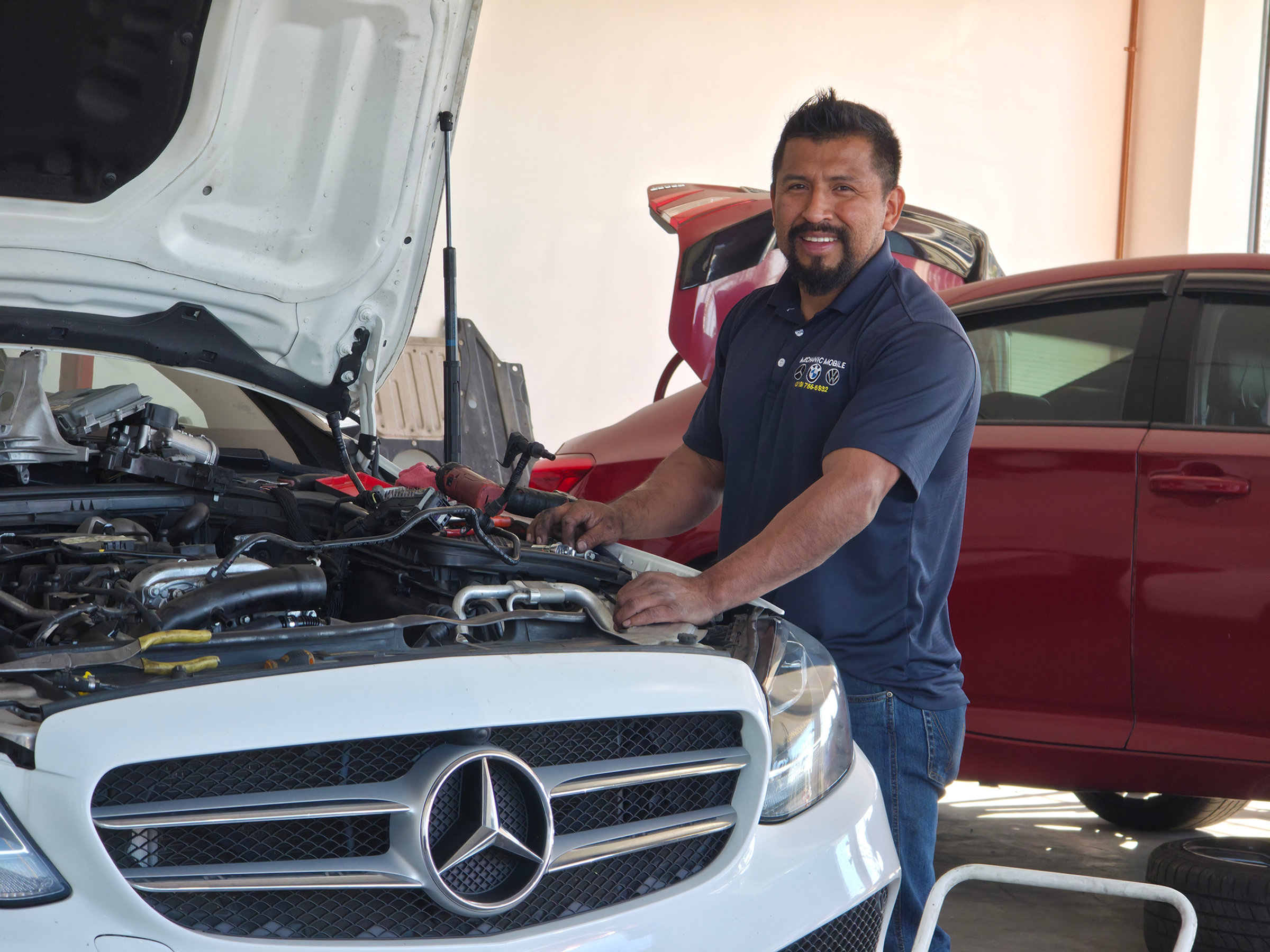 Luis Gonzalez smiling beside a Mercedes-Benz C300 inside the Wilmington shop