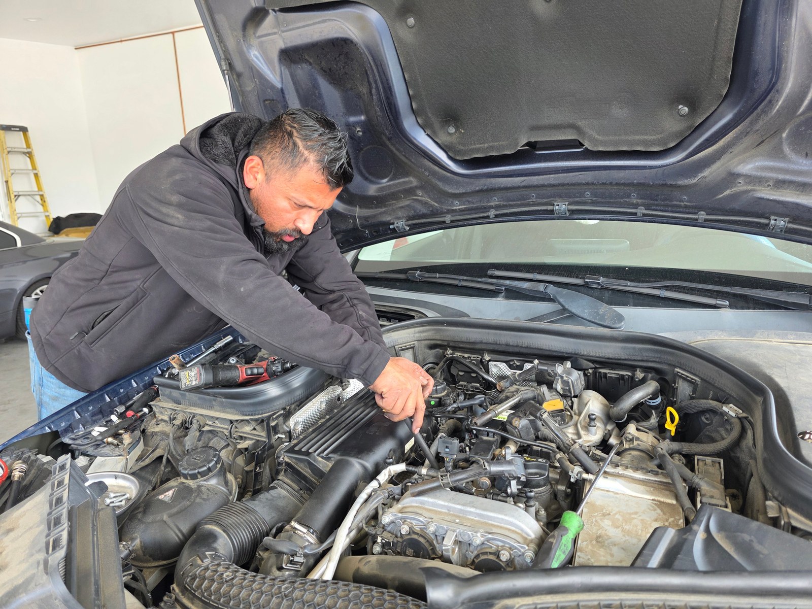Luis Gonzalez trabajando bajo el cofre de un Mercedes-Benz en el taller